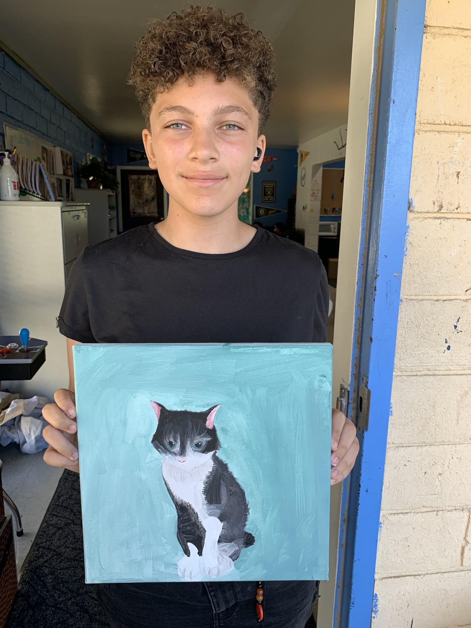 A boy holding a pet portrait he painted of a tabby cat with a white chest