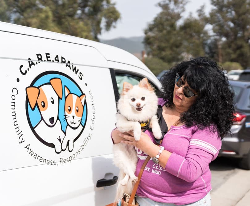 Lady holding her small white dog in front of the C.A.R.E.4Paws Mobile Veterinary Clinic