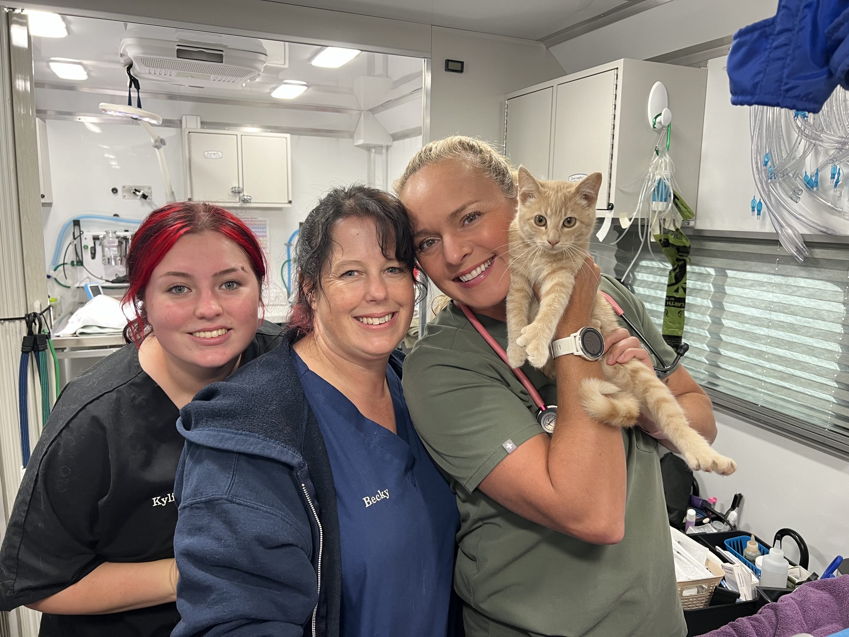 Three C.A.R.E.4Paws vet techs in their scrubs, one is holding an orange cat