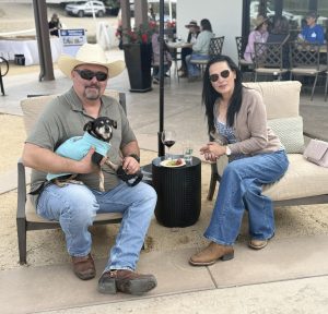 Carlos and Paty Abitia sitting in beige chairs with their small chihuahua