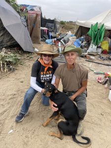 Two C.A.R.E.4Paws volunteers wearing StayPawsitive shirts helping a dog in the Santa Maria riverbed