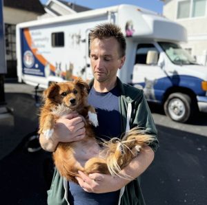 Pet wellness guest posing in front of pet wellness mobile clinic with his golden longhair dog