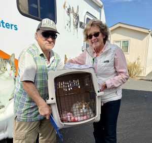 Volunteer and mobile clinic guest holding a large cat carrier with a white and orange cat inside