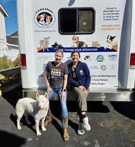 Isabelle Gullo, C.A.R.E.4Paws Executive Director, with her large white dog and new employee sitting at the back of the 26 foot mobile pet wellness clinic that displays sponsors names