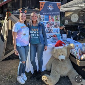Staff members Julia and Libby greeting with a big teddy bear at one of our donation stations