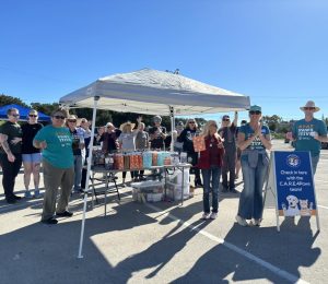 Howliday donation drive thru staff and volunteer team for C.A.R.E.4Paws ringing cow bells and waving hello in invitation to attend