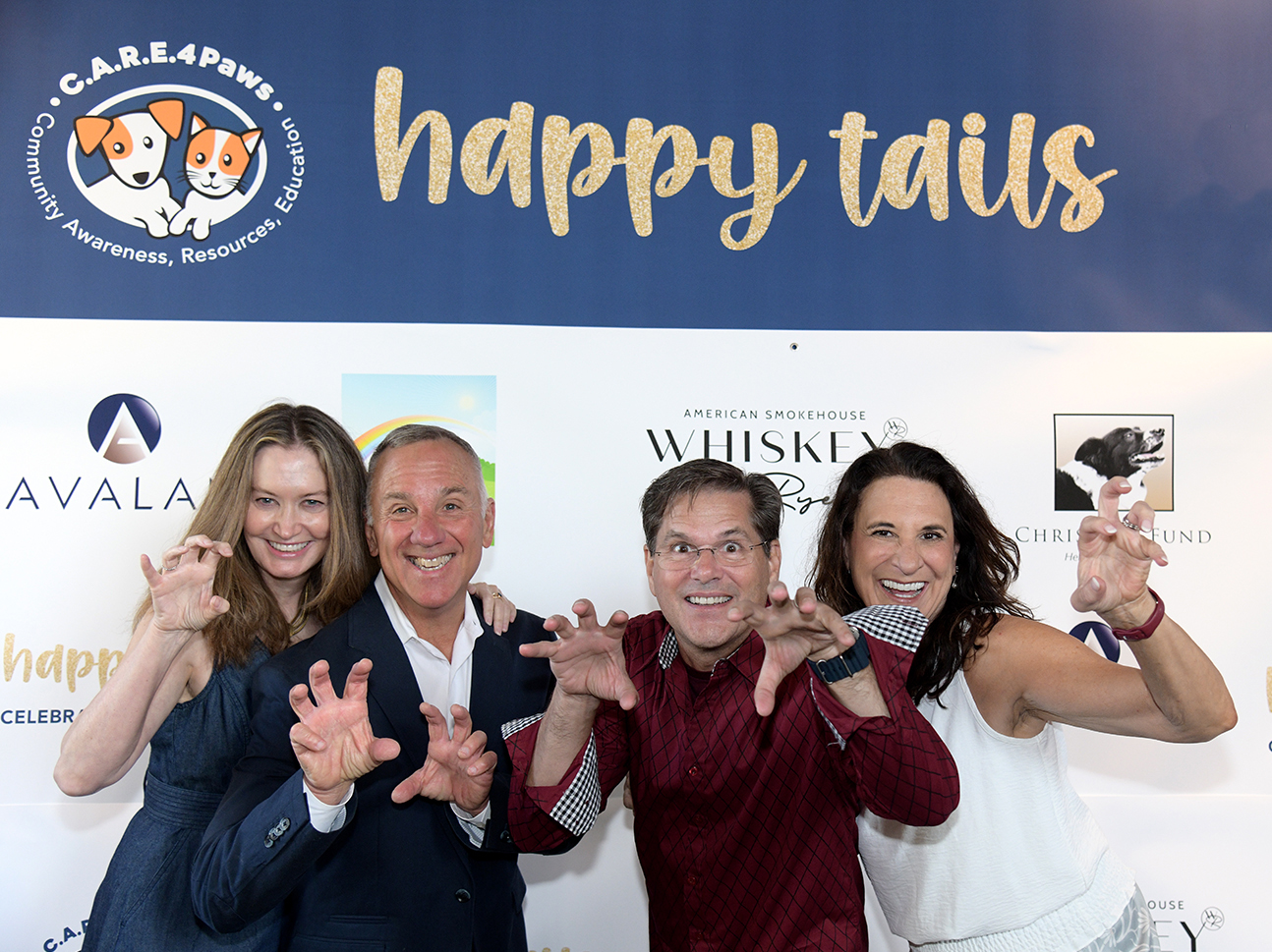 Four C.A.R.E.4Paws Happy Tails Celebration & Fundraiser attendees in front of the event backdrop of sponsors