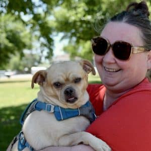 A lady holding her small dog smiling at the camera